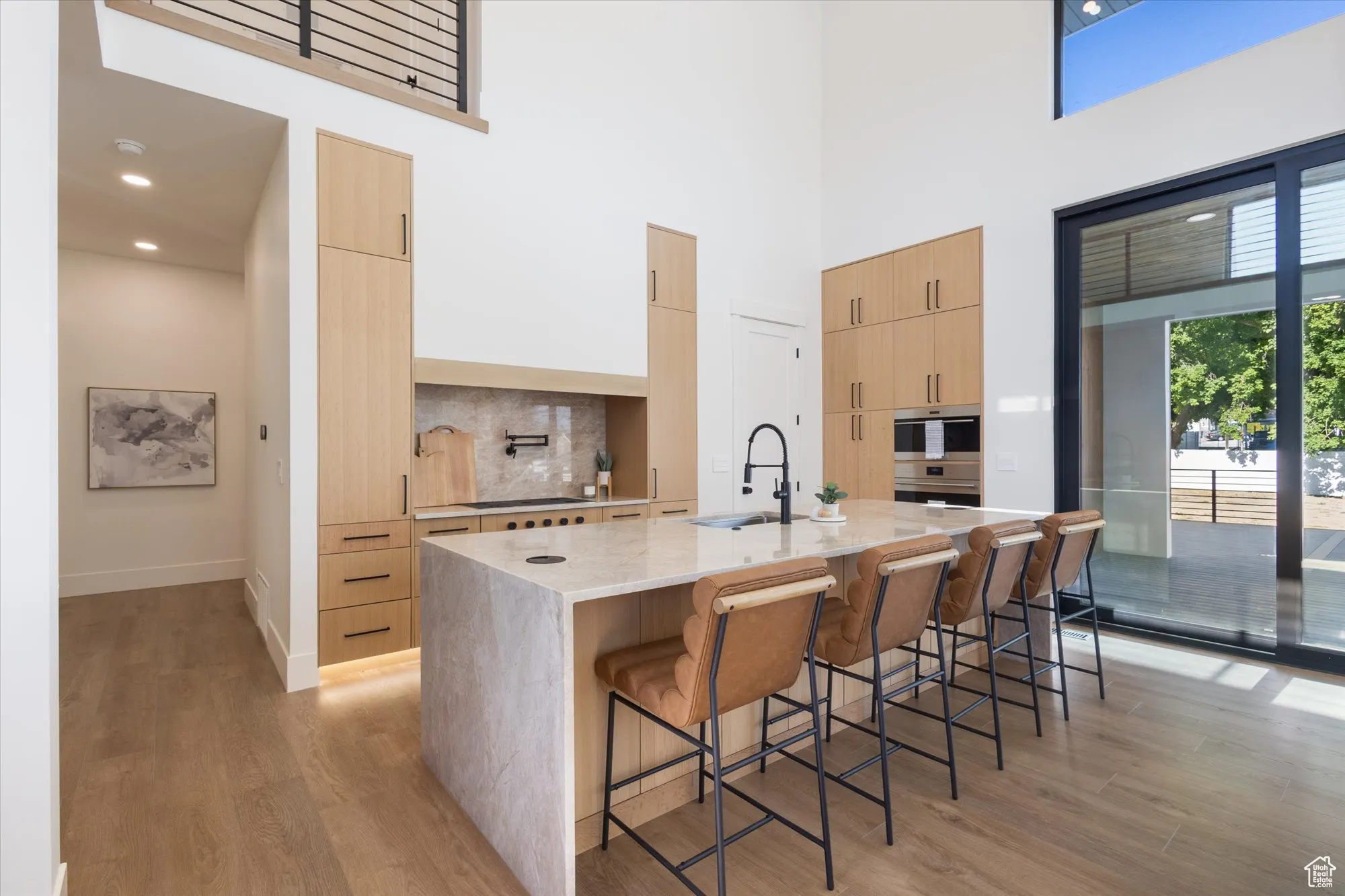 Kitchen featuring modern cabinets, light brown cabinets, light wood-style floors, light stone countertops, and a towering ceiling