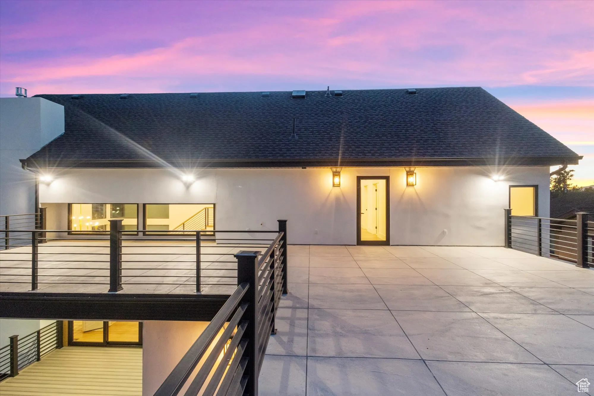 Back of property at dusk with a shingled roof, stucco siding, and a balcony