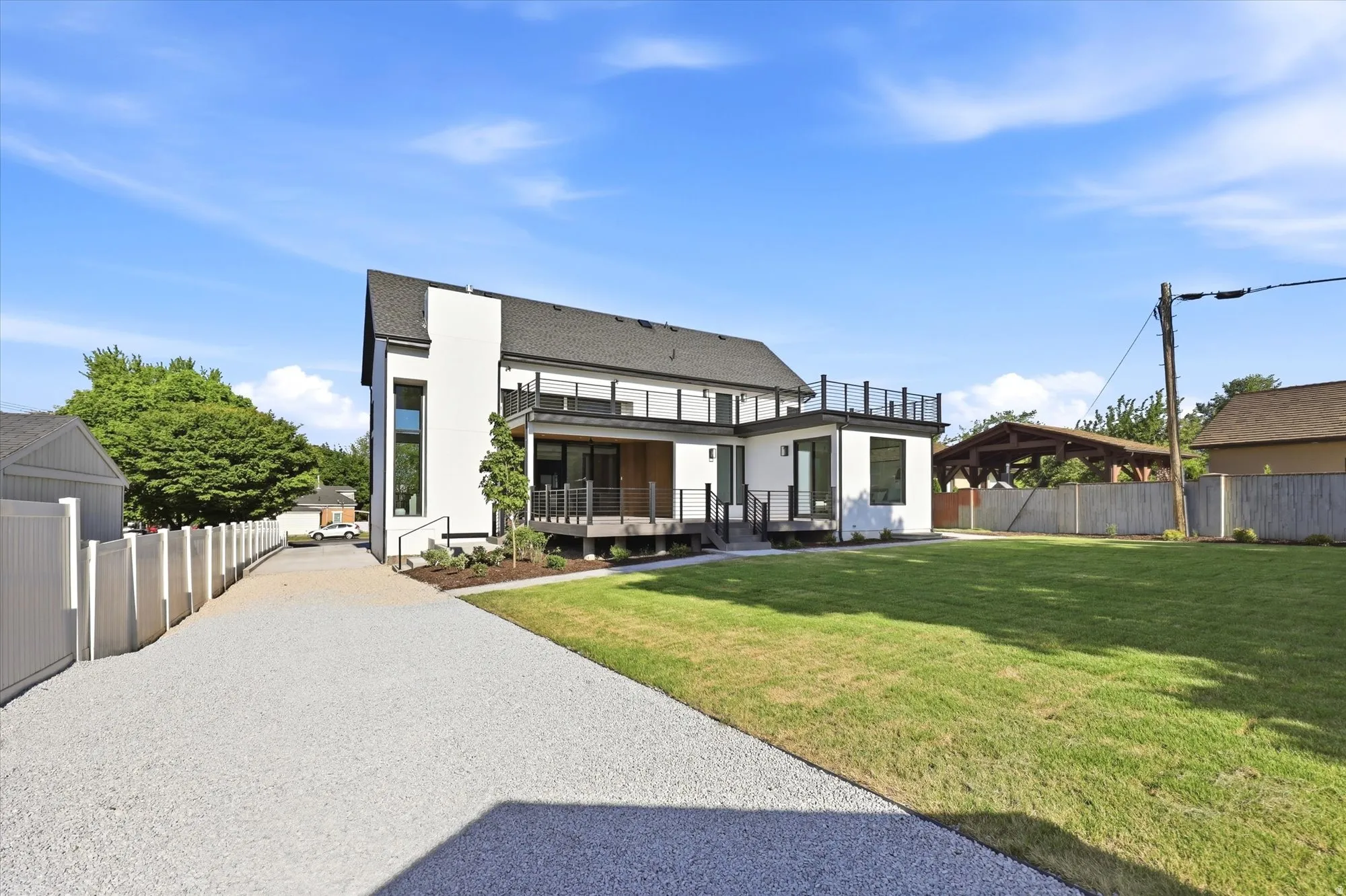 Contemporary architecture featuring a white facade with dark trim, multiple decks with black railings, and a gravel driveway