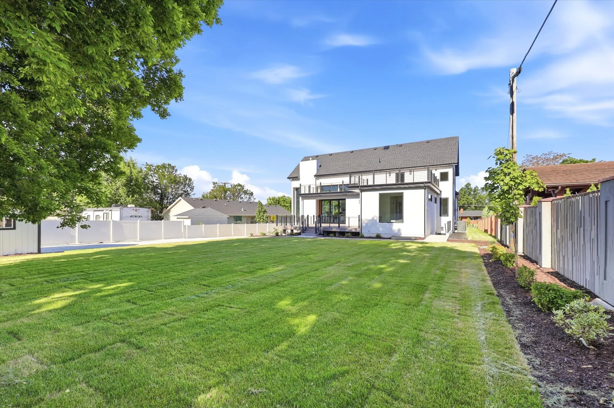 Expansive lawn space featuring a modern white exterior with dark-framed windows, a second-story balcony, and a ground-level deck