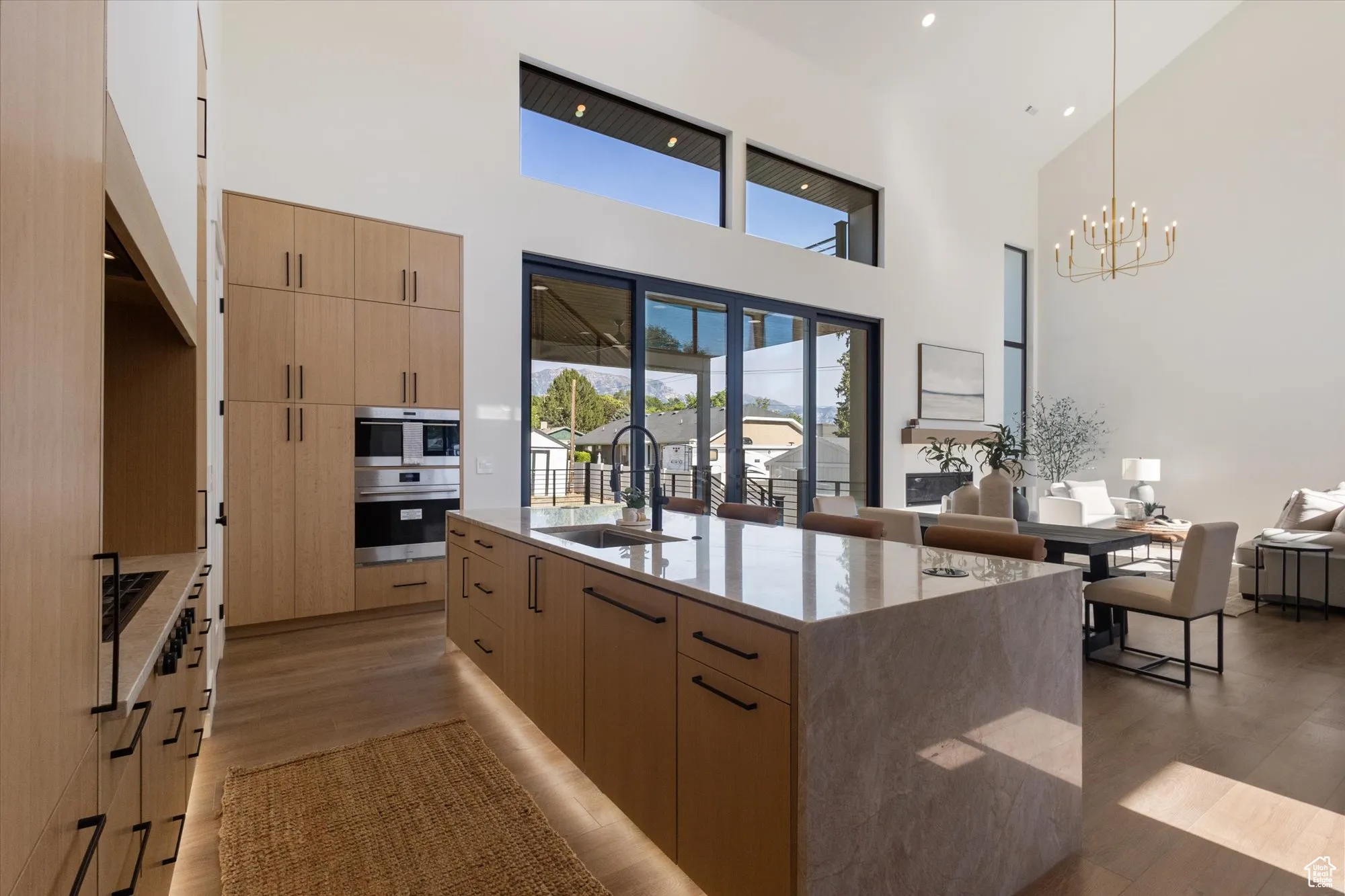 Kitchen with light brown cabinetry, modern cabinets, open floor plan, light wood-type flooring, and a towering ceiling
