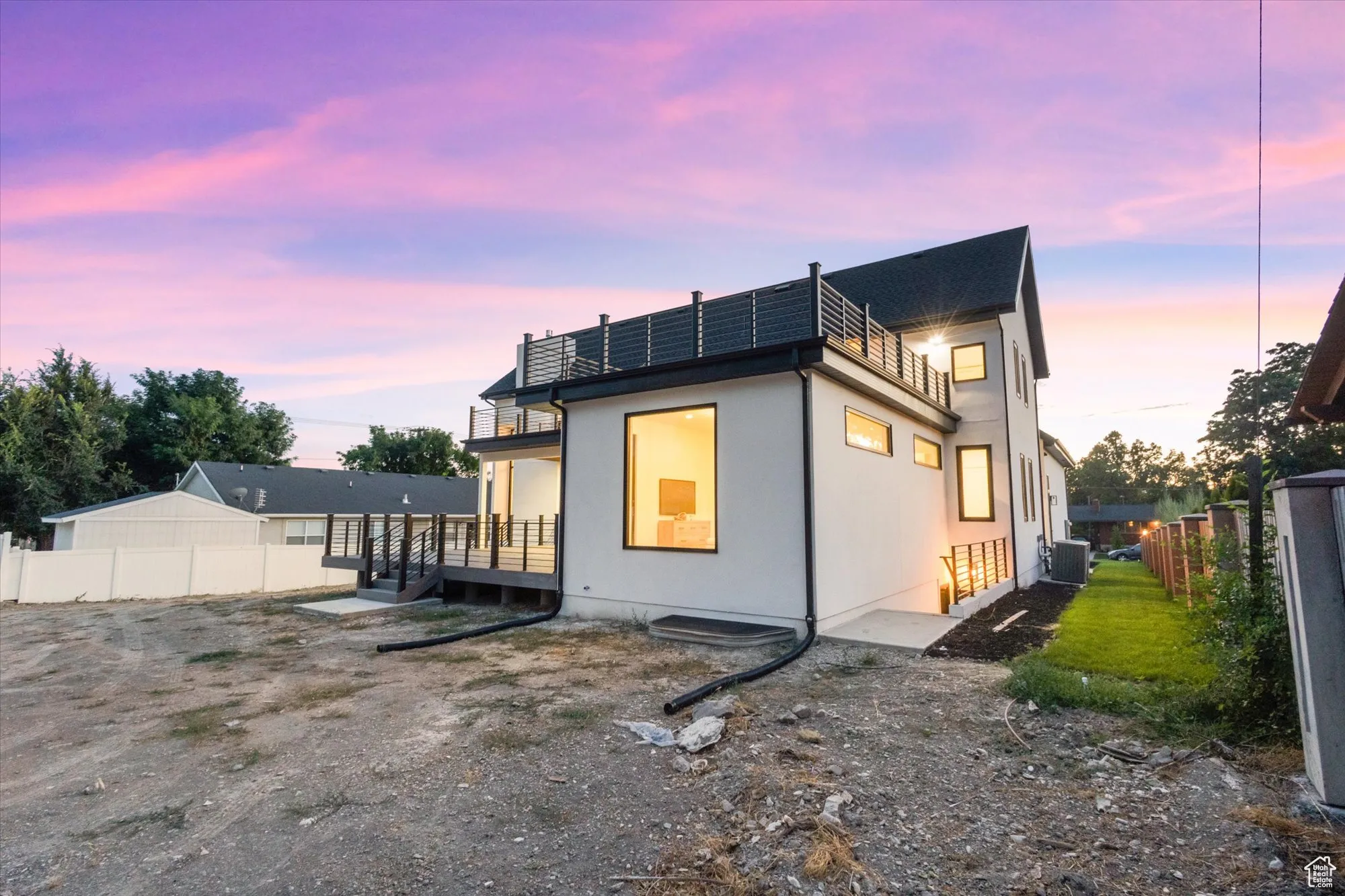 Back of property at dusk with a fenced backyard, solar panels, a balcony, and a deck