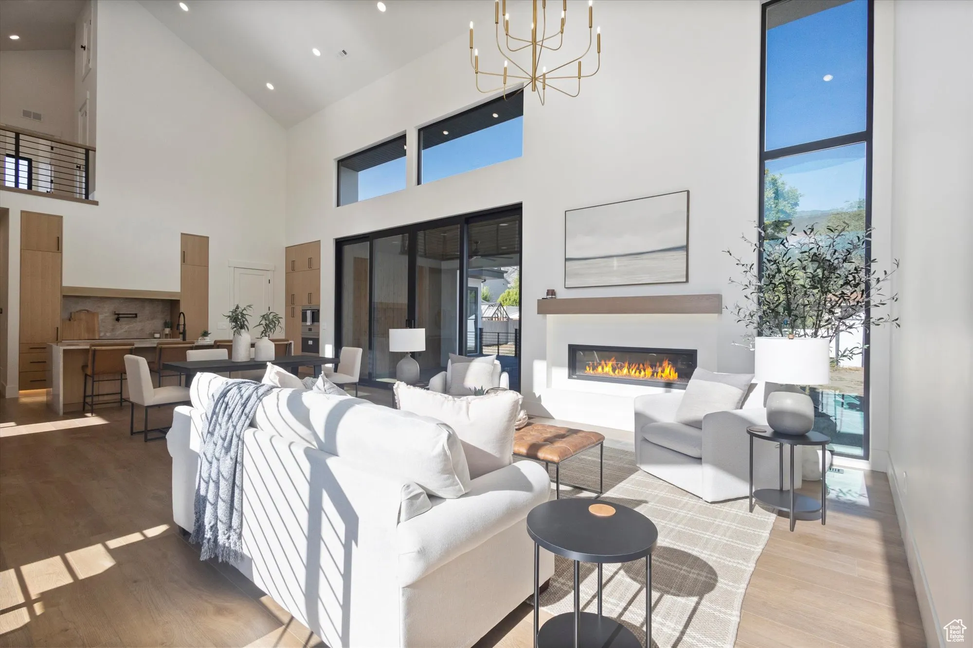 Living room featuring wood finished floors, a glass covered fireplace, high vaulted ceiling, healthy amount of natural light, and a chandelier