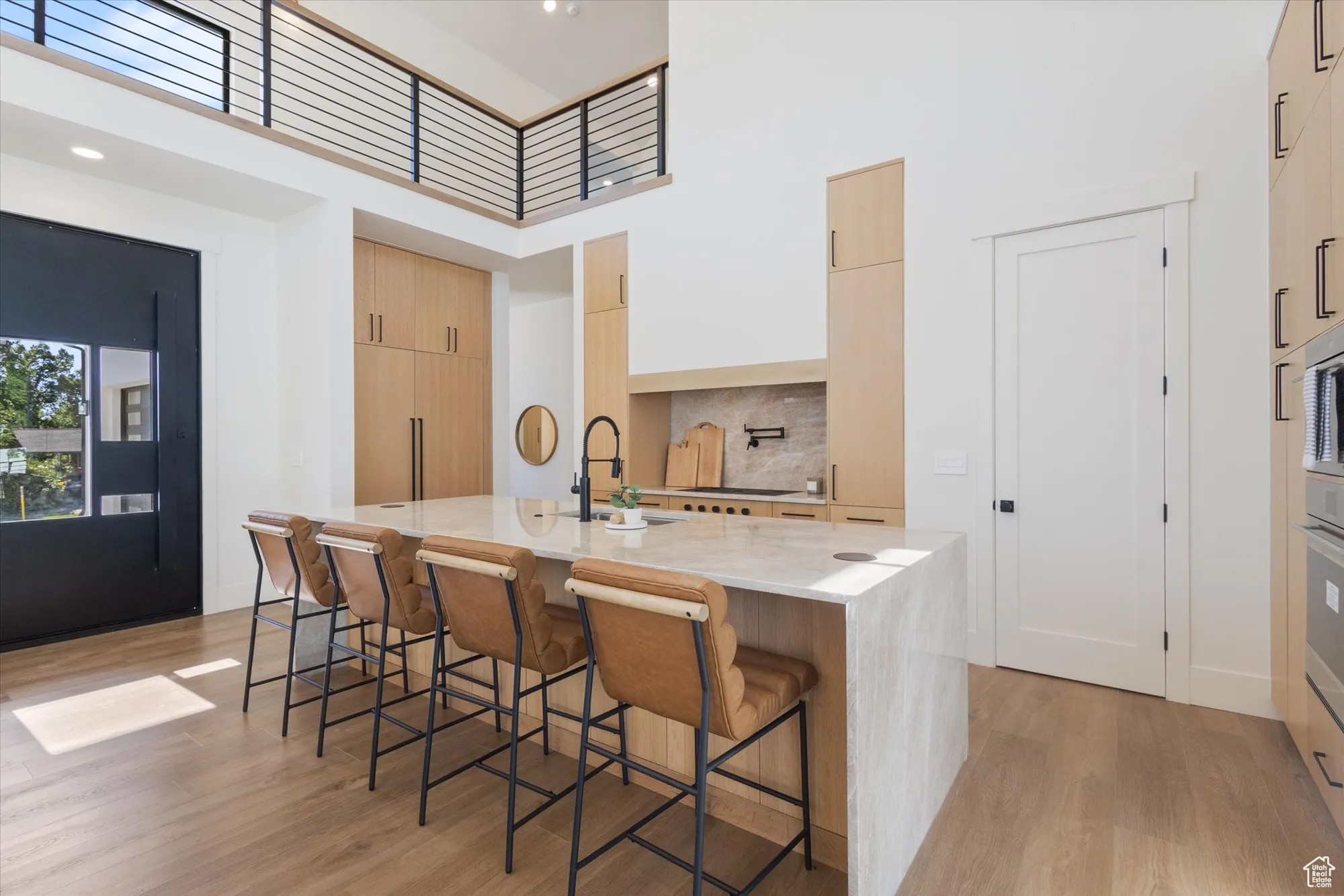 Kitchen with modern cabinets, a towering ceiling, light wood finished floors, a kitchen bar, and light stone countertops
