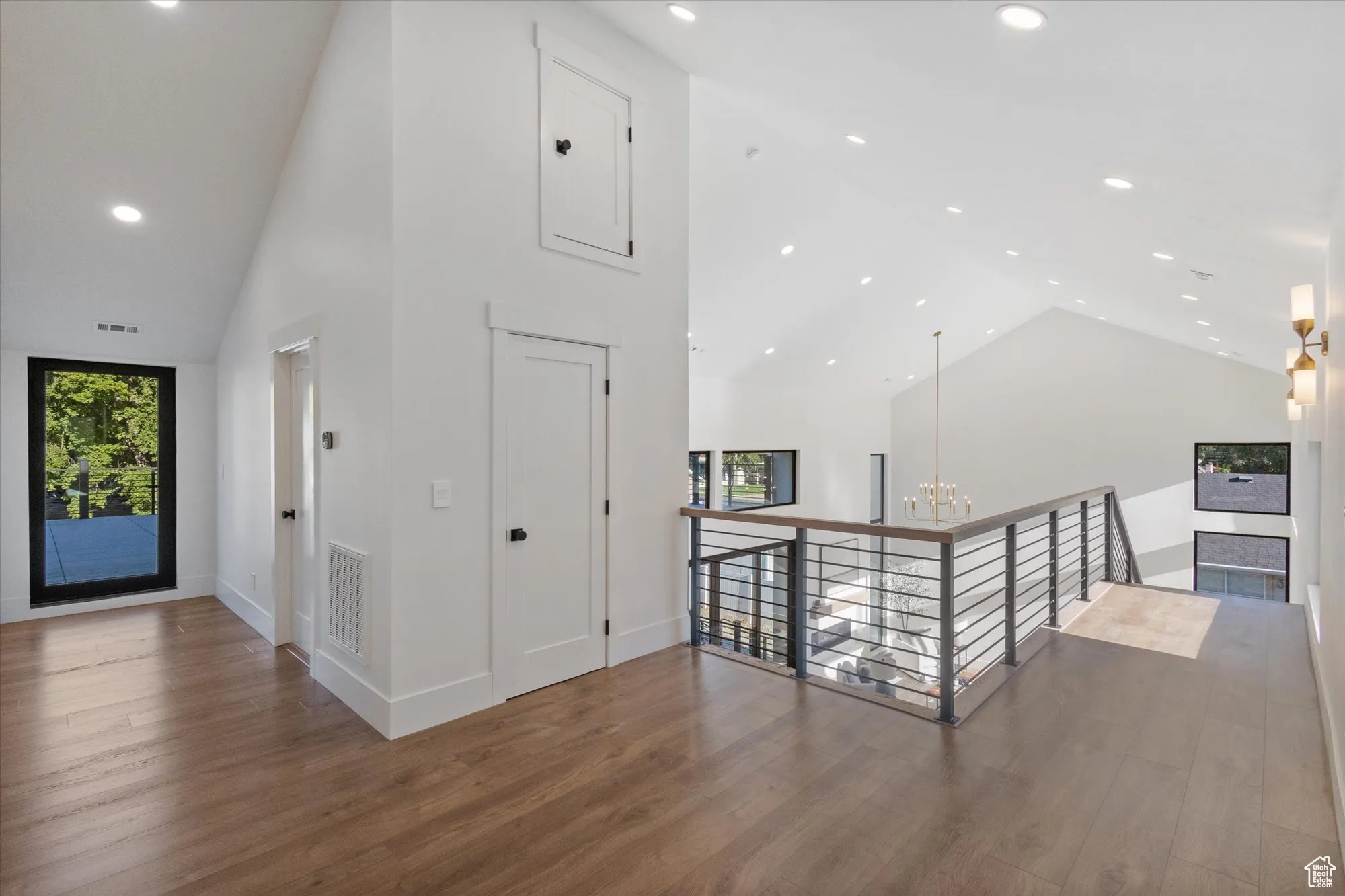 Hallway with high vaulted ceiling, wood finished floors, recessed lighting, an upstairs landing, and a chandelier