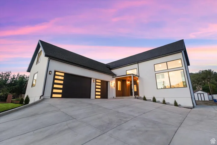 Contemporary house with an attached garage, concrete driveway, a shingled roof, and stucco siding