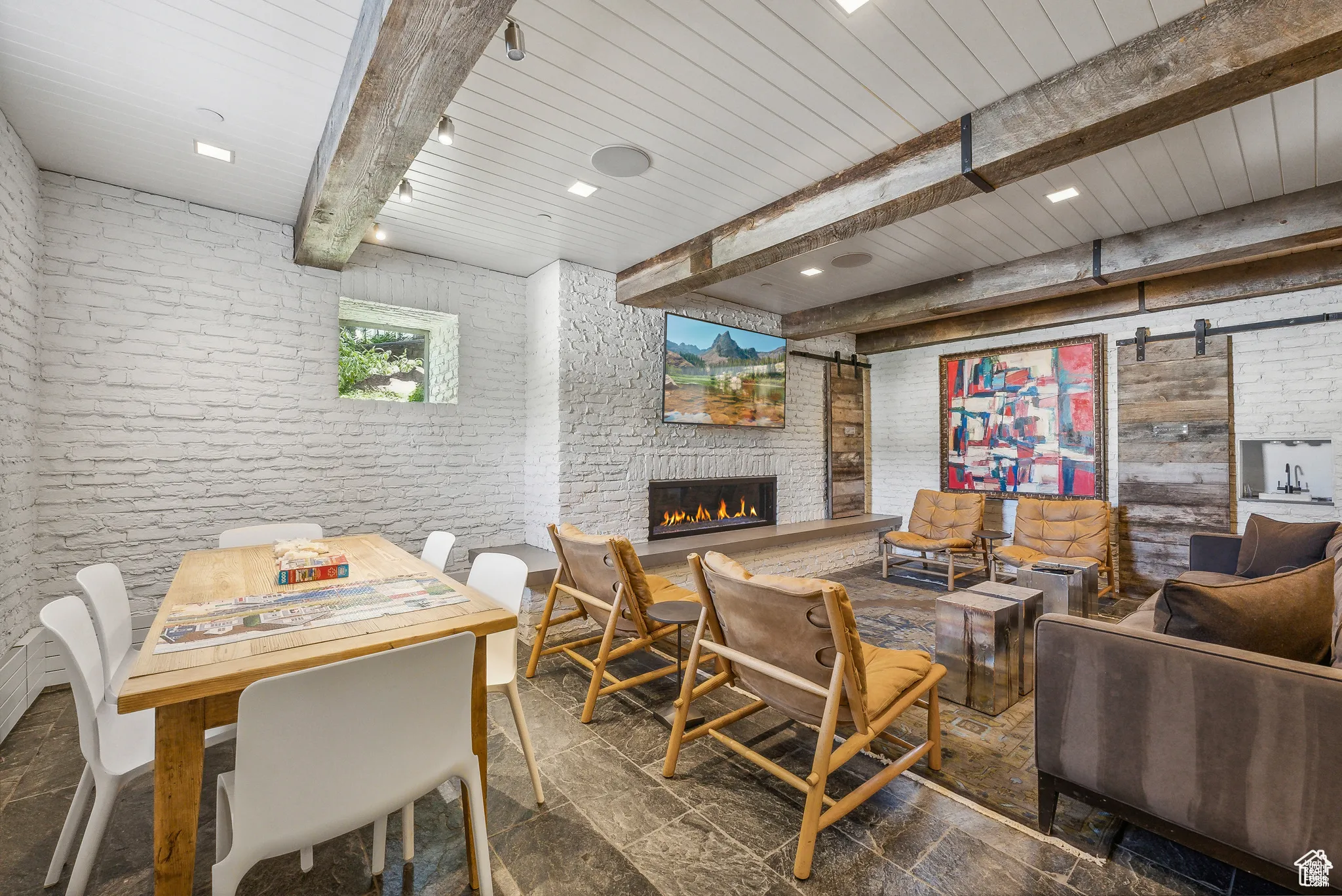 Living area with a barn door, brick wall, beam ceiling, a large fireplace, and recessed lighting