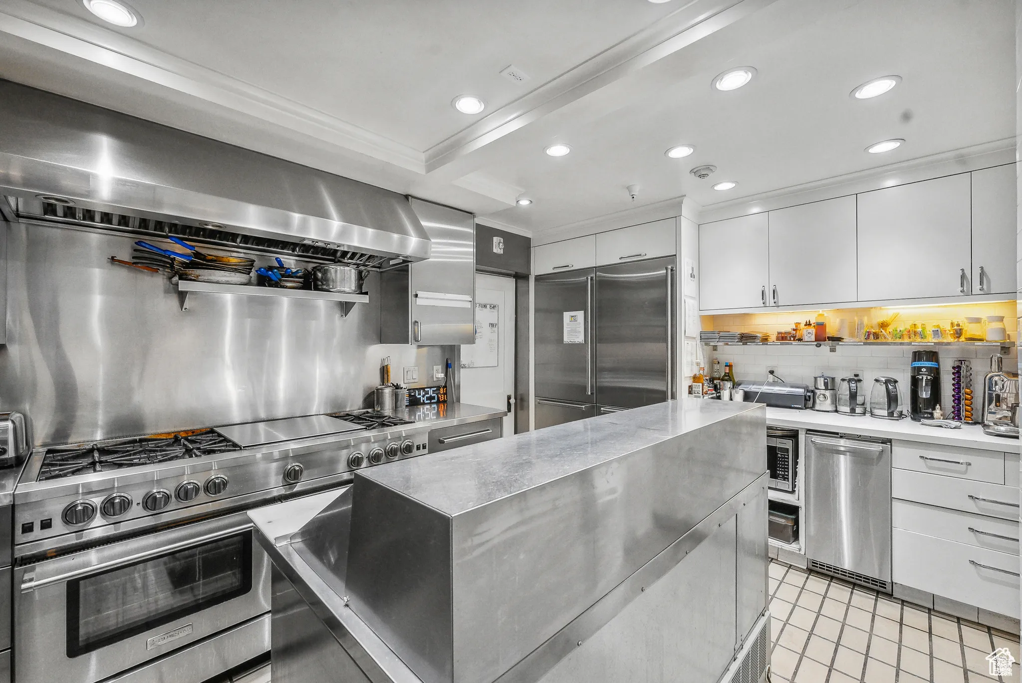 Kitchen featuring high end appliances, backsplash, recessed lighting, white cabinetry, and range hood