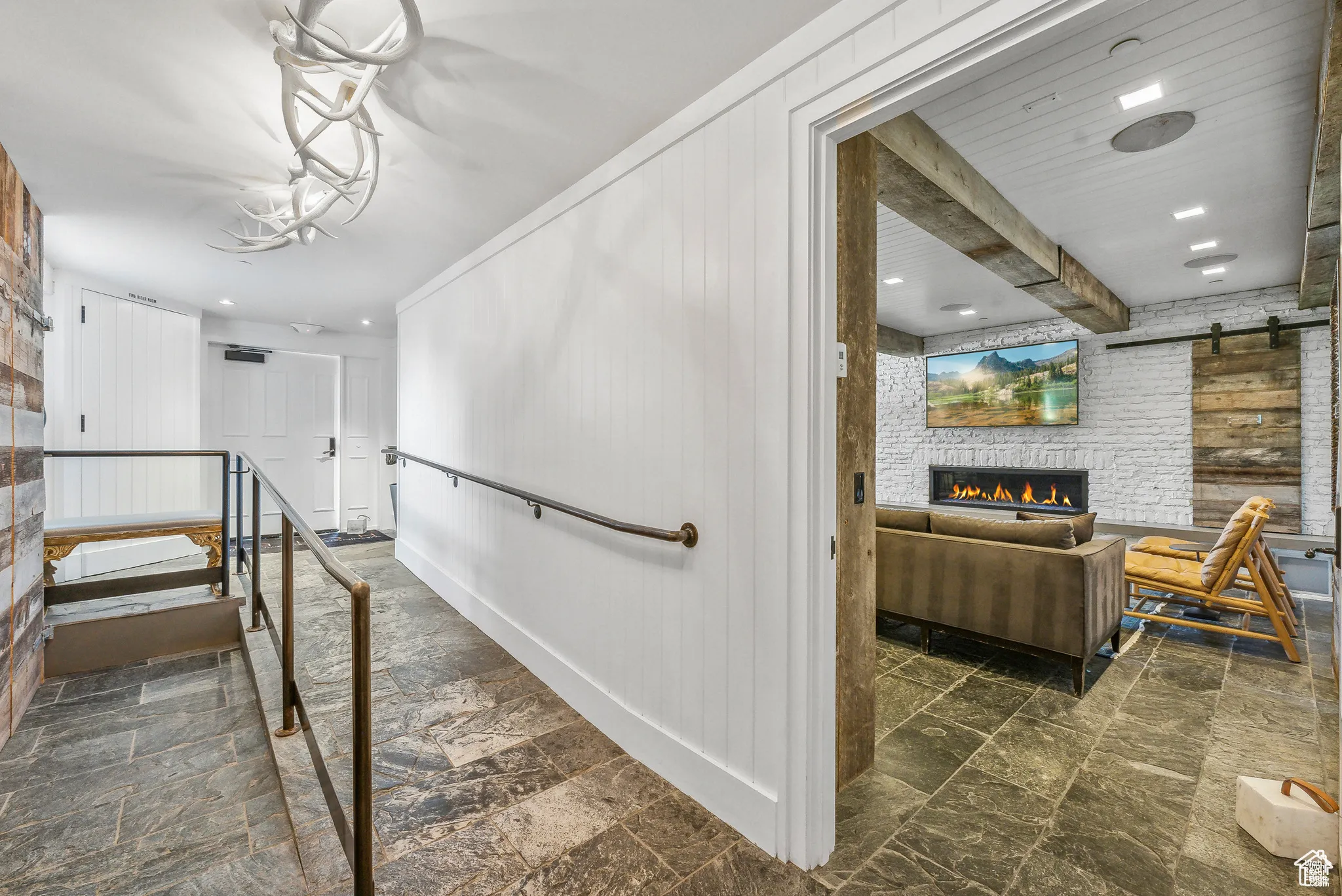 Staircase with stone finish floors, a barn door, a brick fireplace, recessed lighting, and beamed ceiling