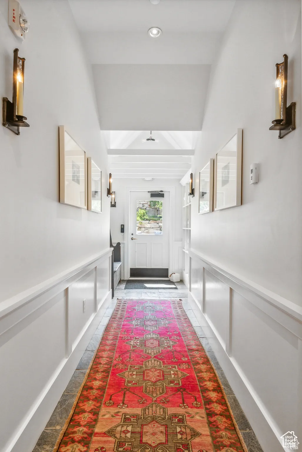 Doorway to outside with a decorative wall, wainscoting, and beamed ceiling