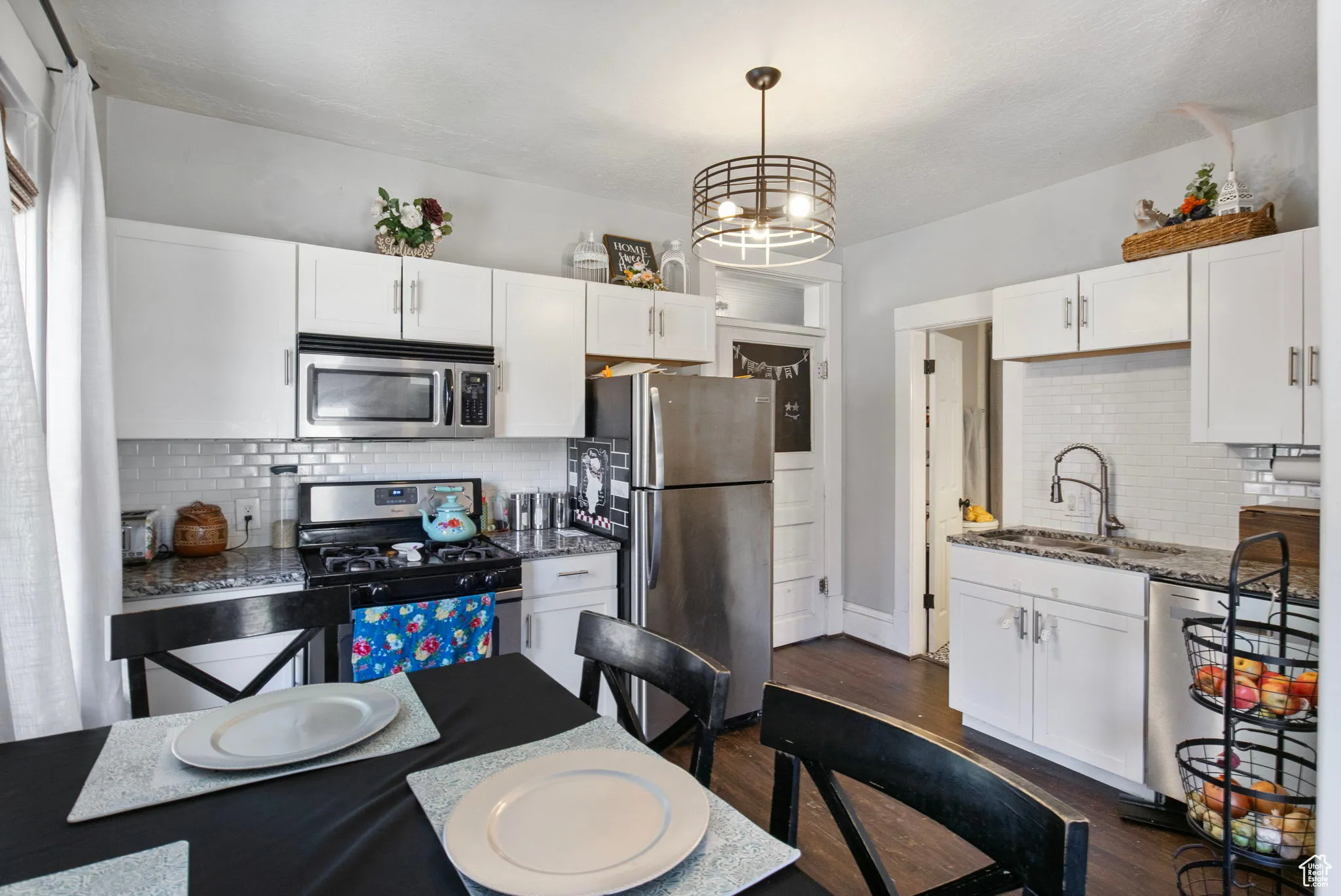 Kitchen featuring decorative backsplash, stainless steel appliances, dark wood finished floors, white cabinetry, and dark stone countertops