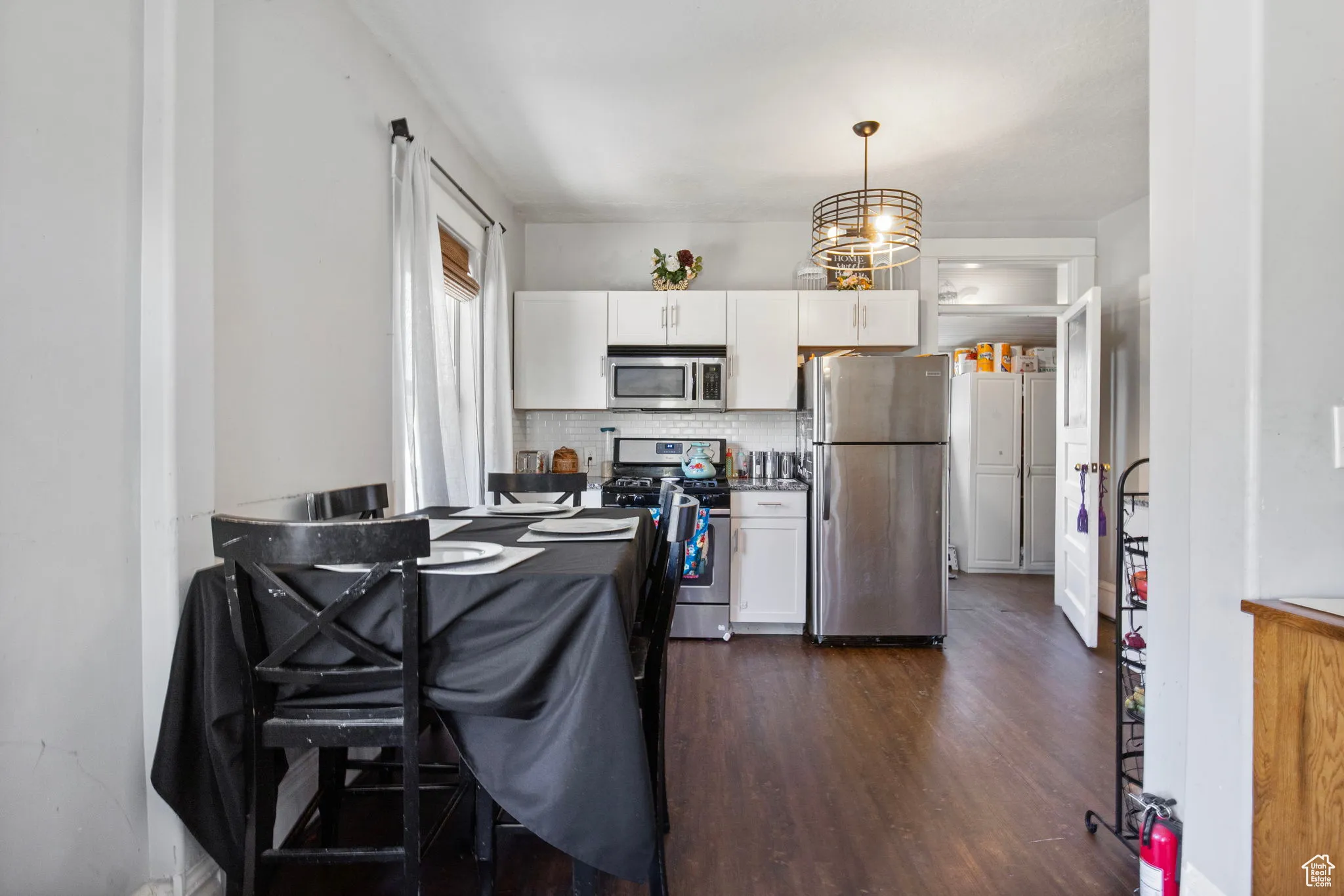 Kitchen with appliances with stainless steel finishes, dark wood-style floors, white cabinets, and decorative backsplash