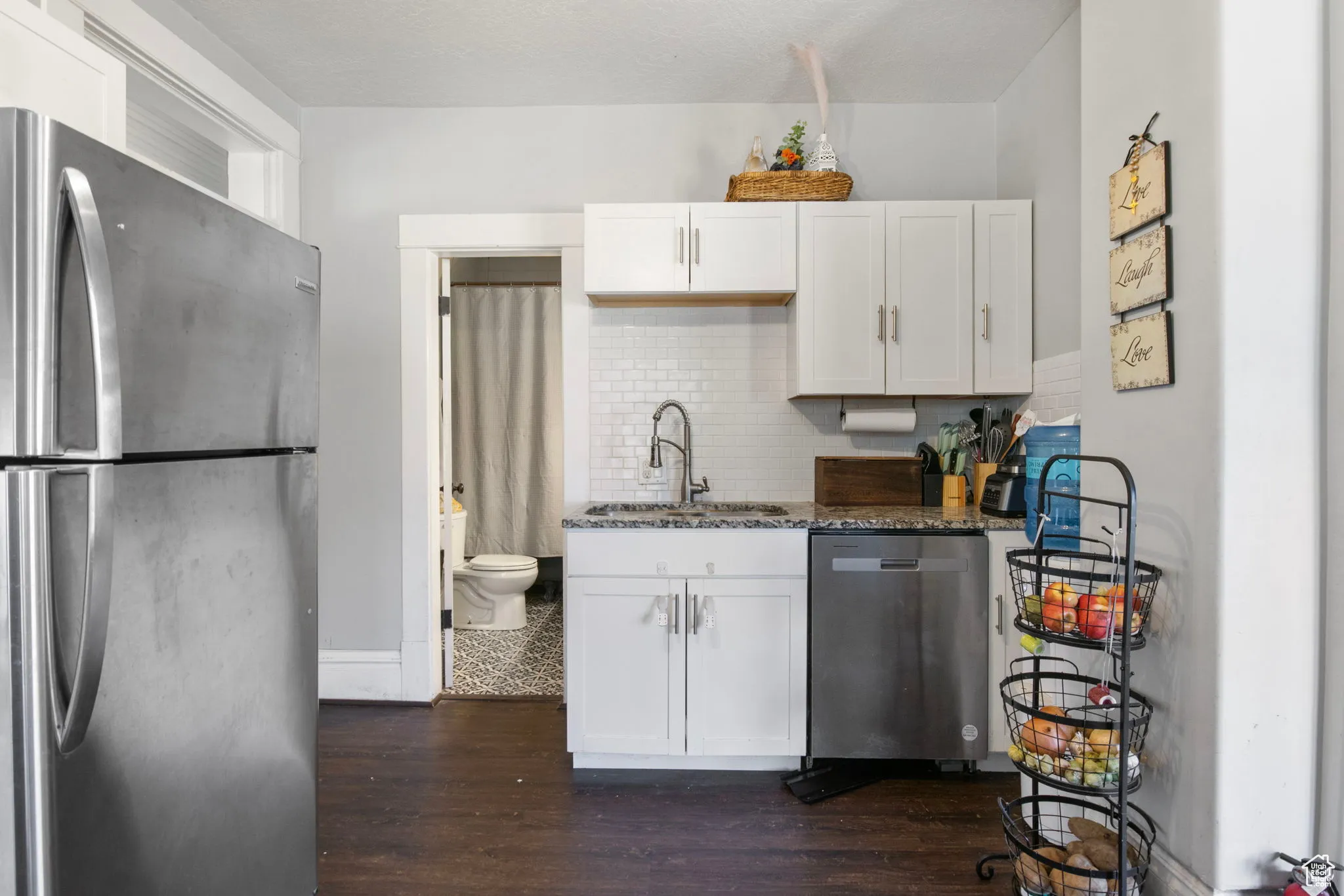 Kitchen featuring appliances with stainless steel finishes, dark stone counters, dark wood-style floors, white cabinets, and tasteful backsplash