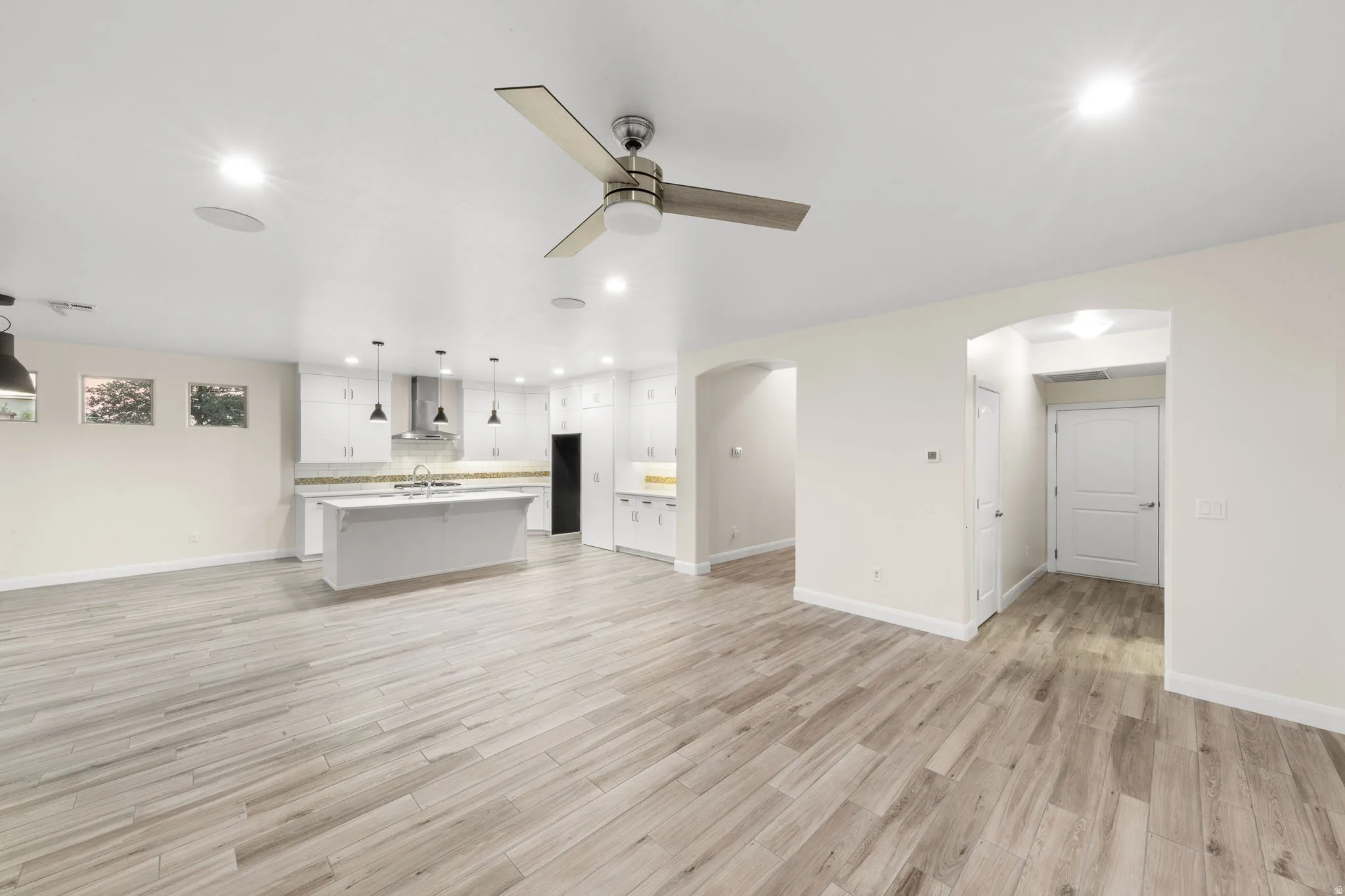 Unfurnished living room featuring arched walkways, recessed lighting, light wood finished floors, and ceiling fan