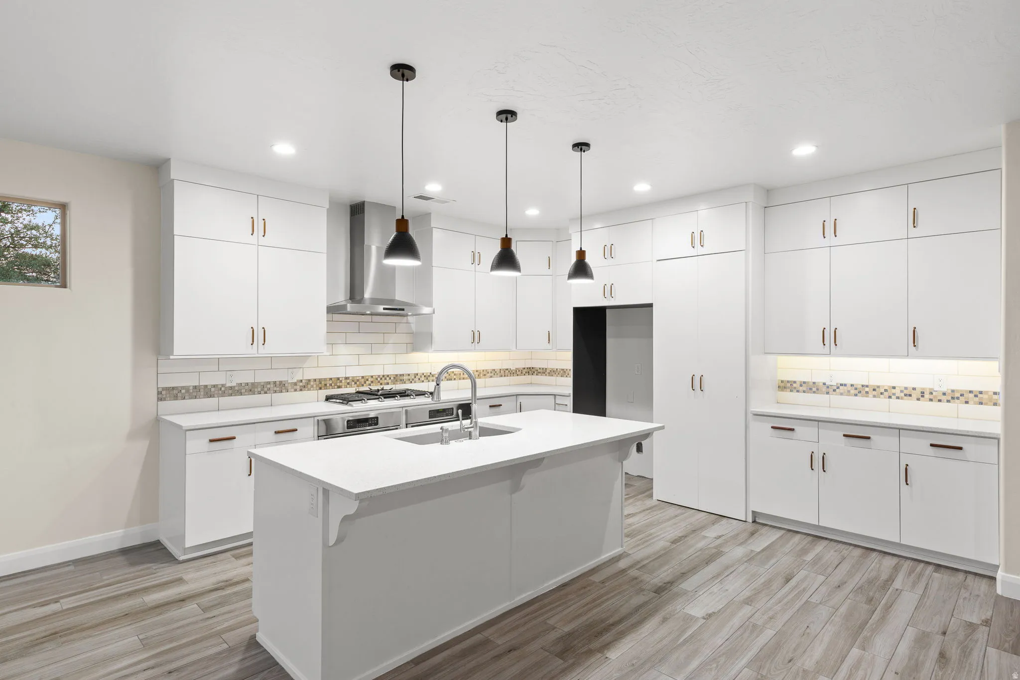 Kitchen featuring white cabinetry, wall chimney range hood, hanging light fixtures, a breakfast bar, and recessed lighting