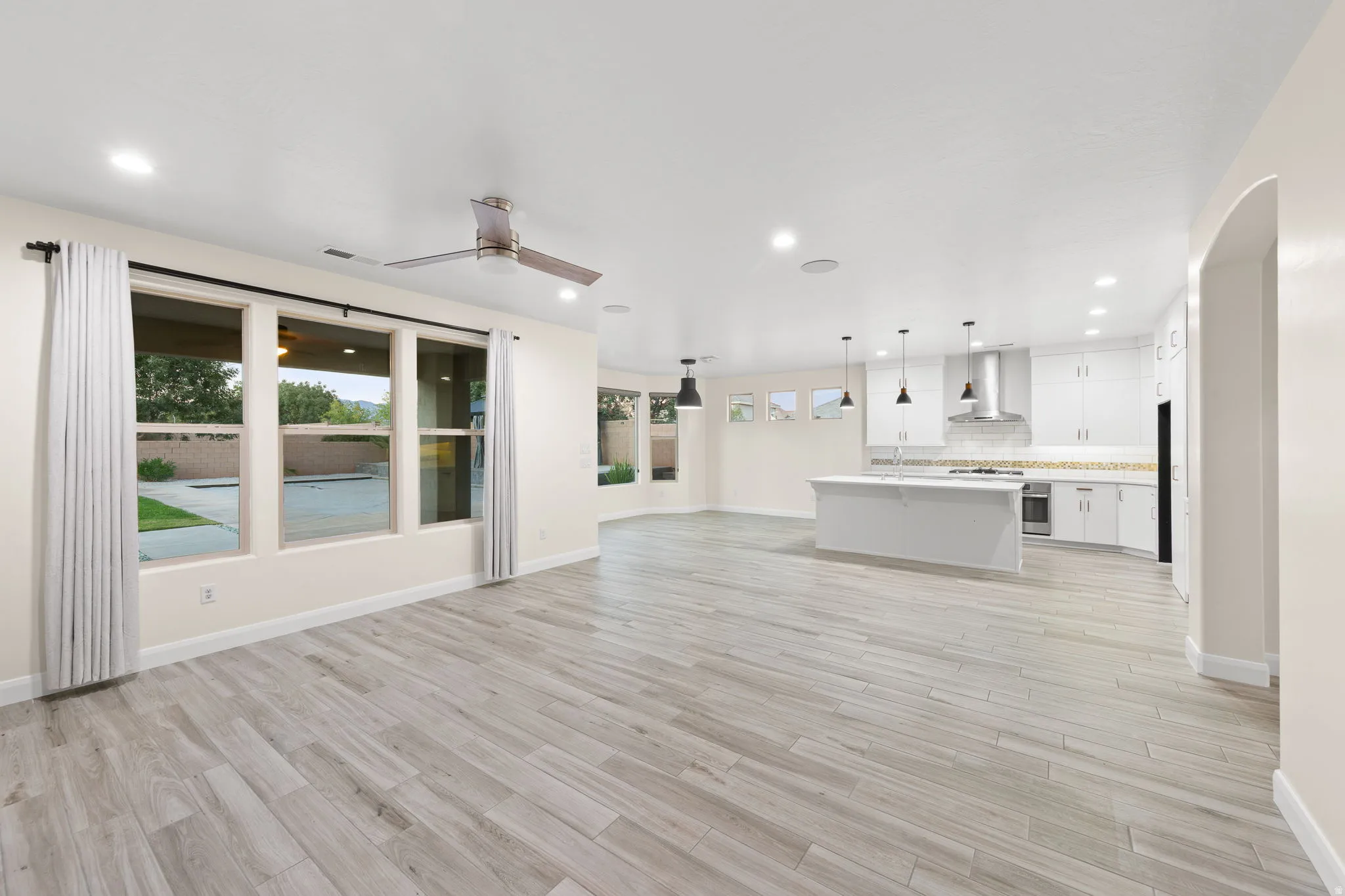 Unfurnished living room with recessed lighting, light wood finished floors, ceiling fan, and arched walkways