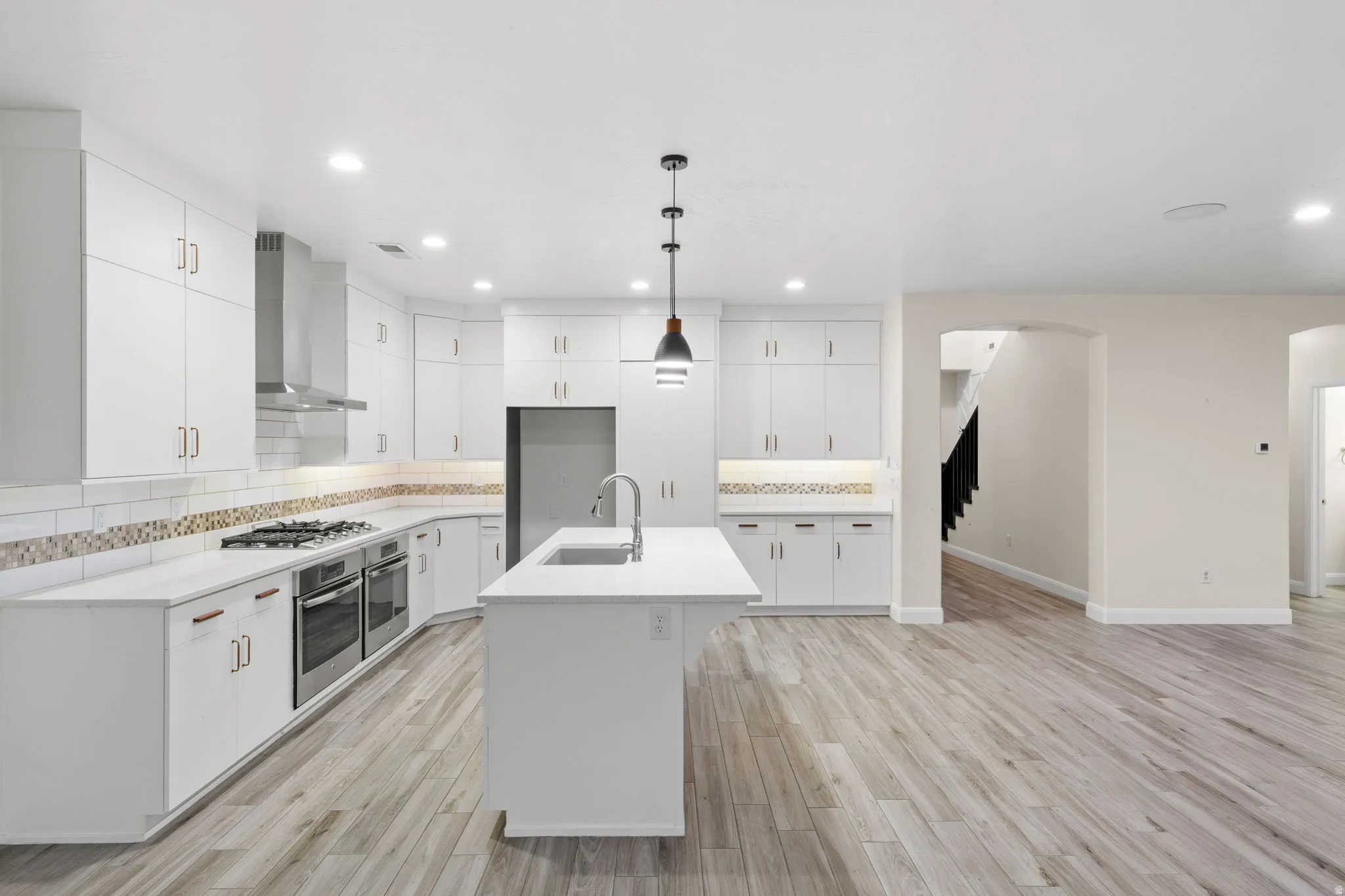Kitchen with backsplash, wall chimney range hood, hanging light fixtures, white cabinetry, and recessed lighting