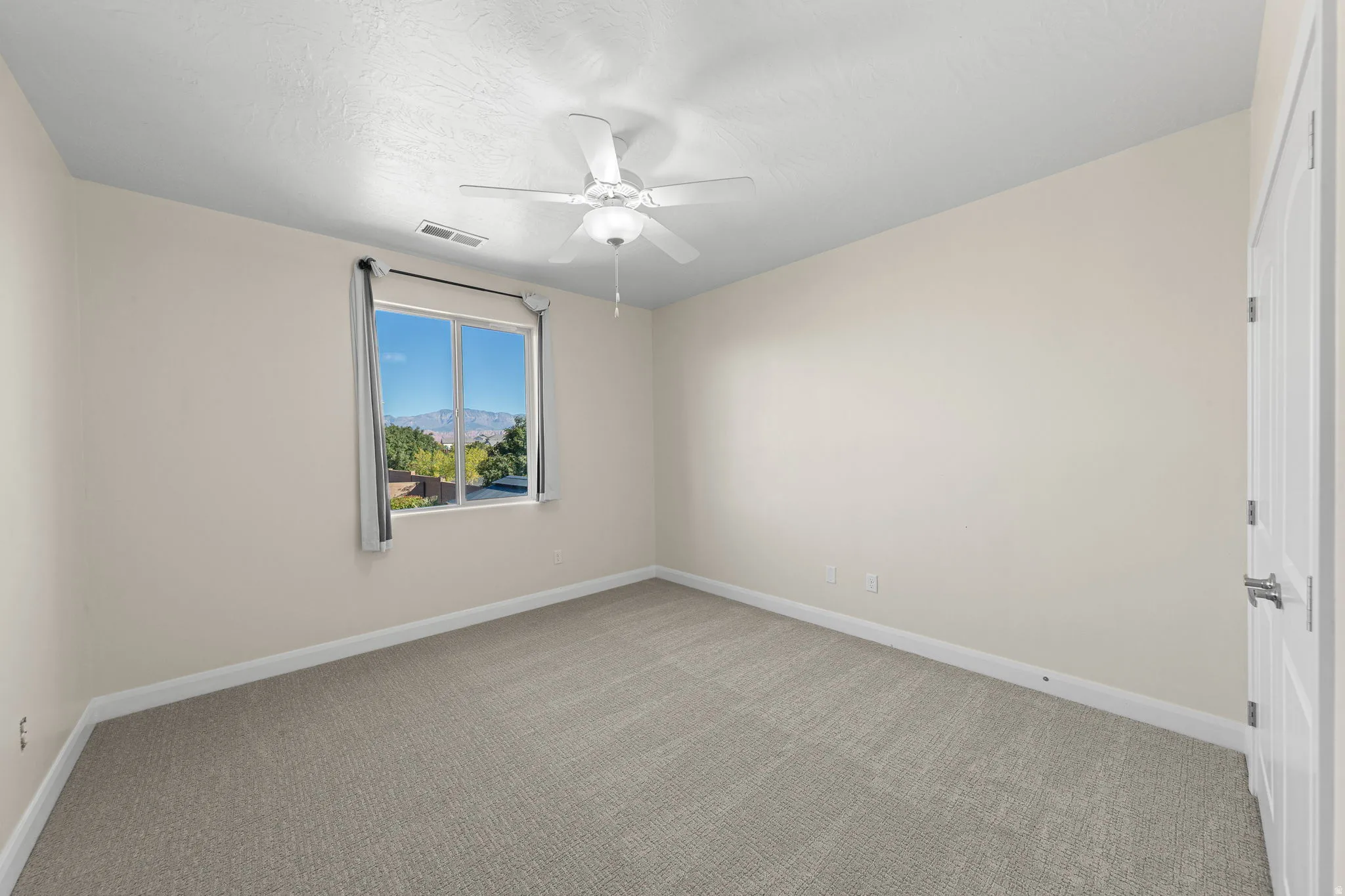 Empty room with light carpet, a ceiling fan, a mountain view, and a textured ceiling