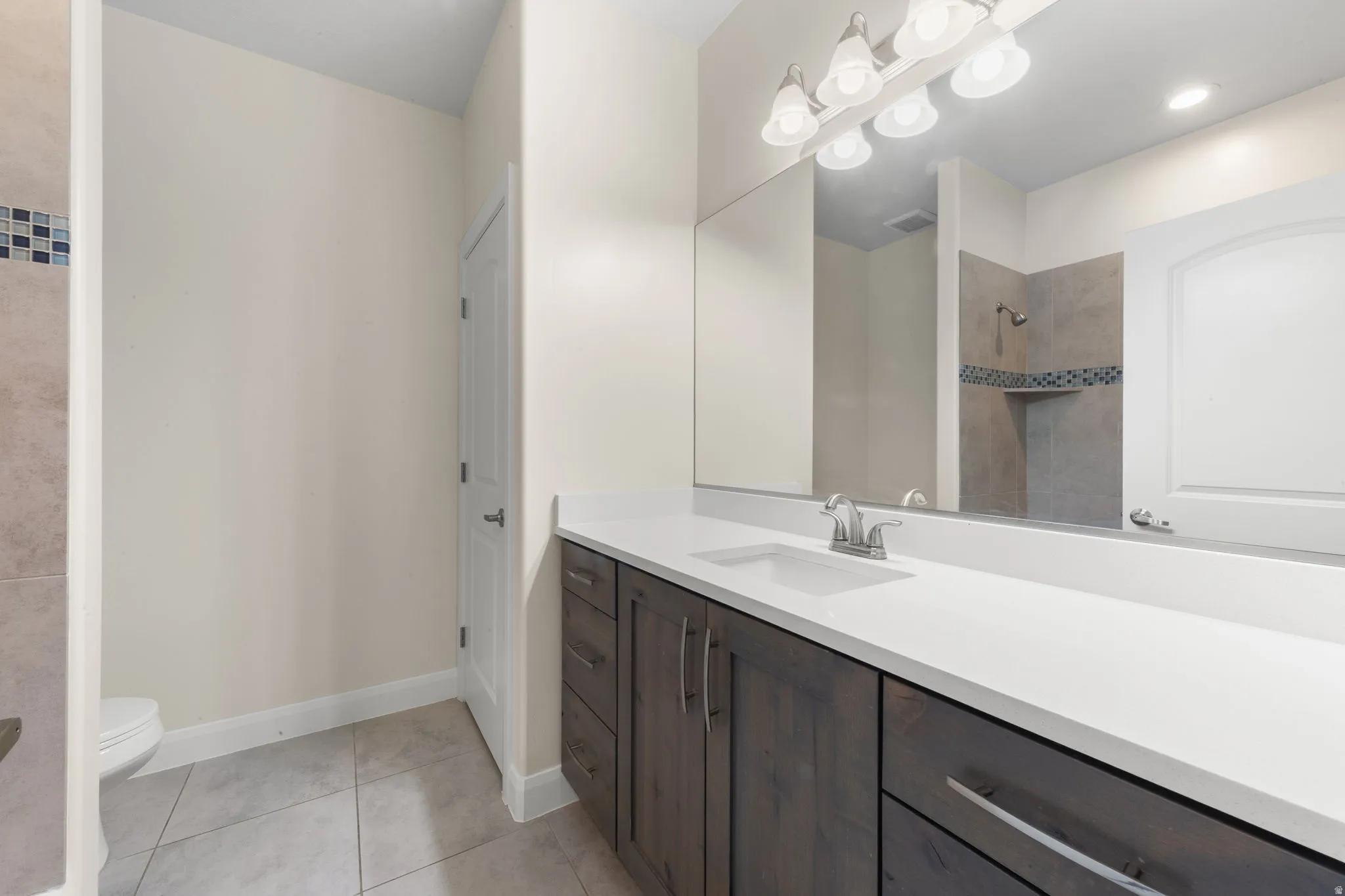 Full bathroom with vanity, tiled shower, and light tile patterned floors