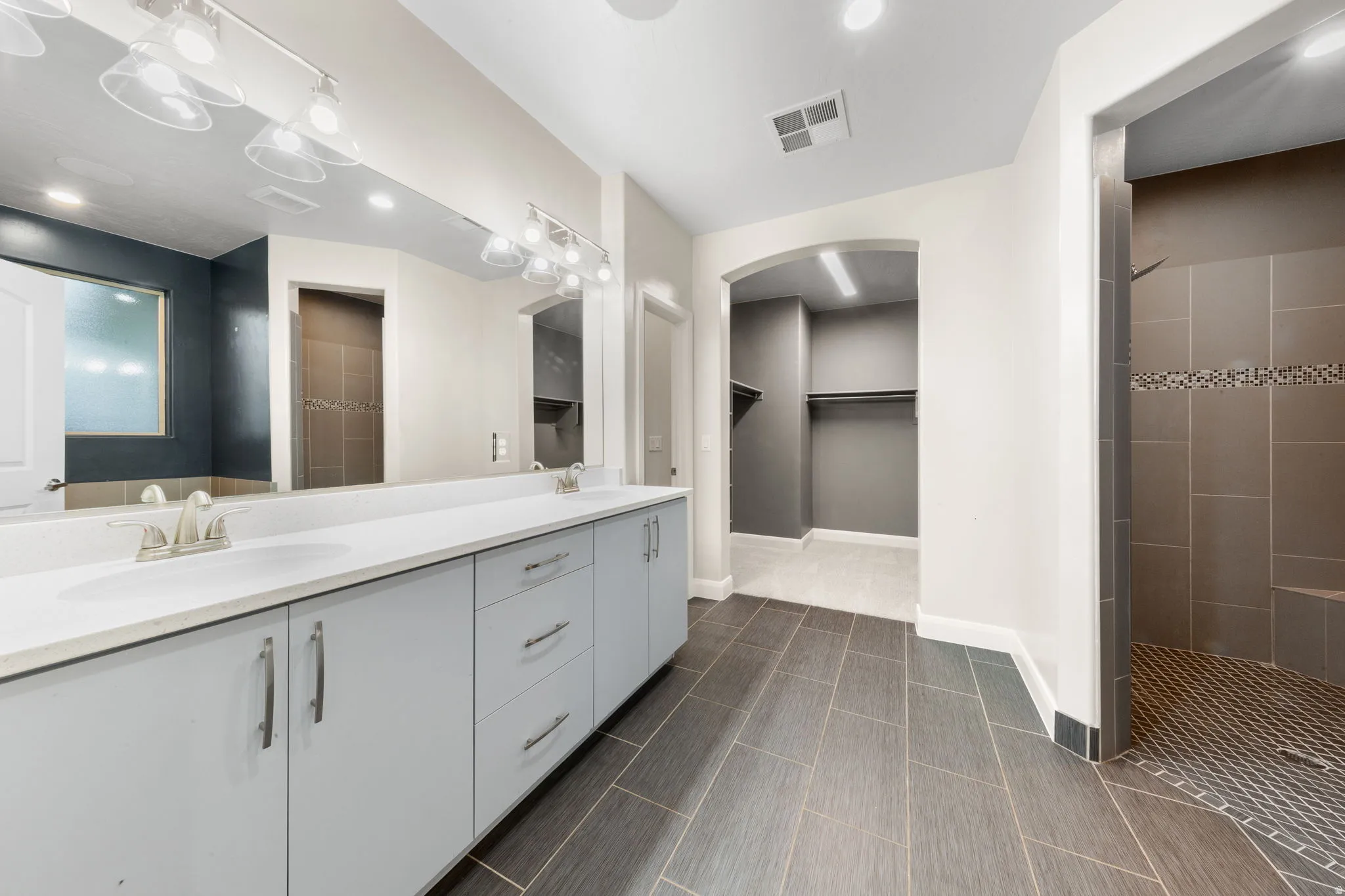 Full bathroom with a spacious closet, double vanity, tiled shower, and recessed lighting