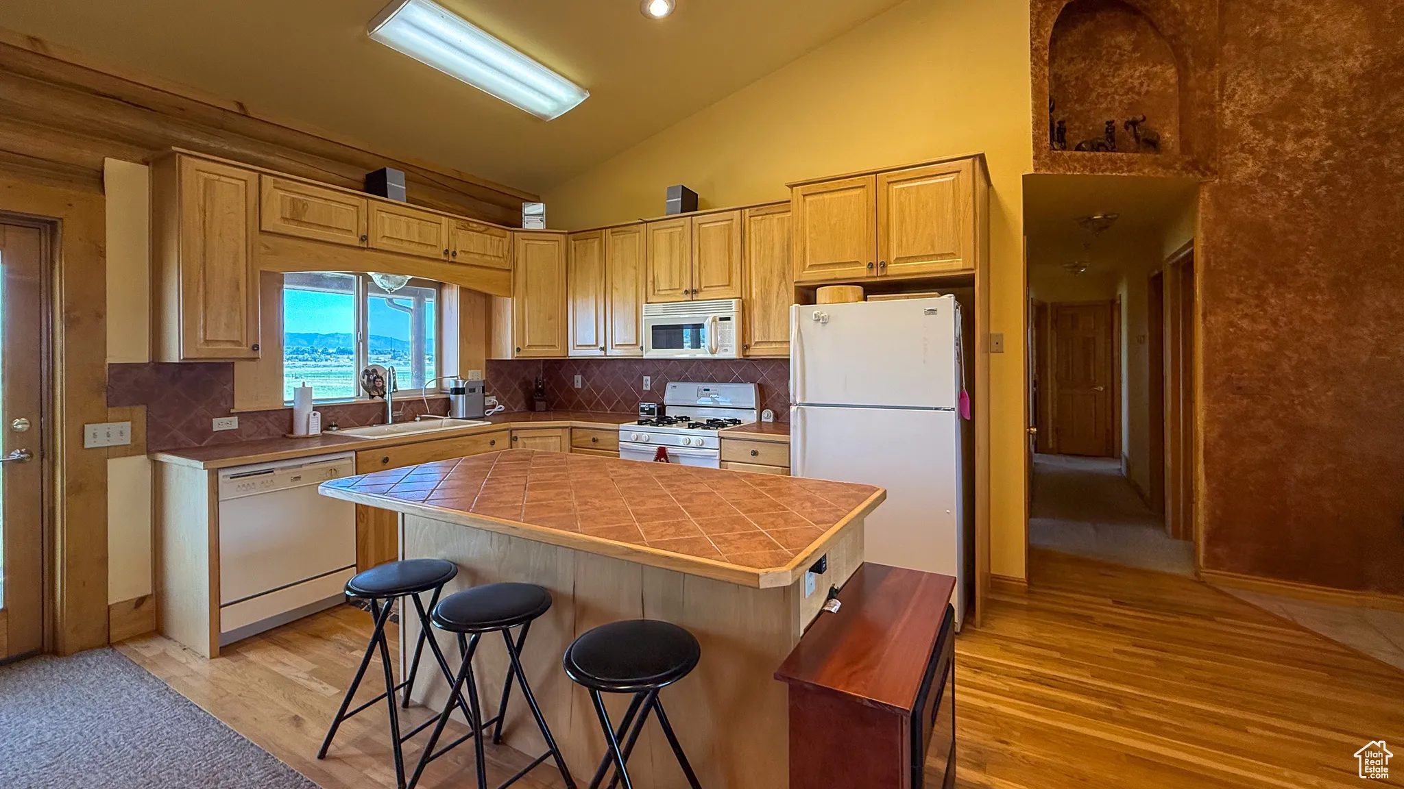 Kitchen with white appliances, high vaulted ceiling, a breakfast bar area, light wood-type flooring, and a kitchen island