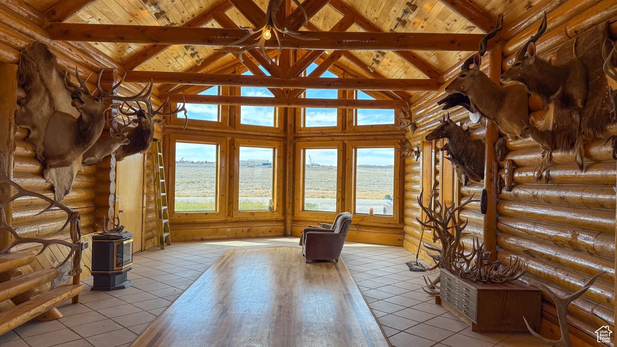 Unfurnished living room with log walls, a wooden ceiling with exposed beams, high vaulted ceiling, and light tile patterned floors
