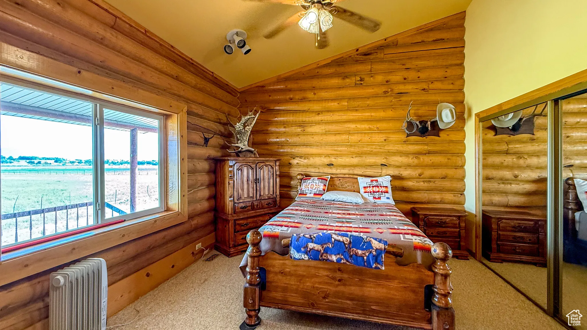 Carpeted bedroom with vaulted ceiling, radiator heating unit, ceiling fan, and rustic walls