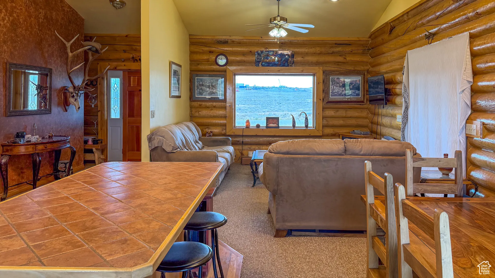 Carpeted living room with rustic walls, ceiling fan, and vaulted ceiling