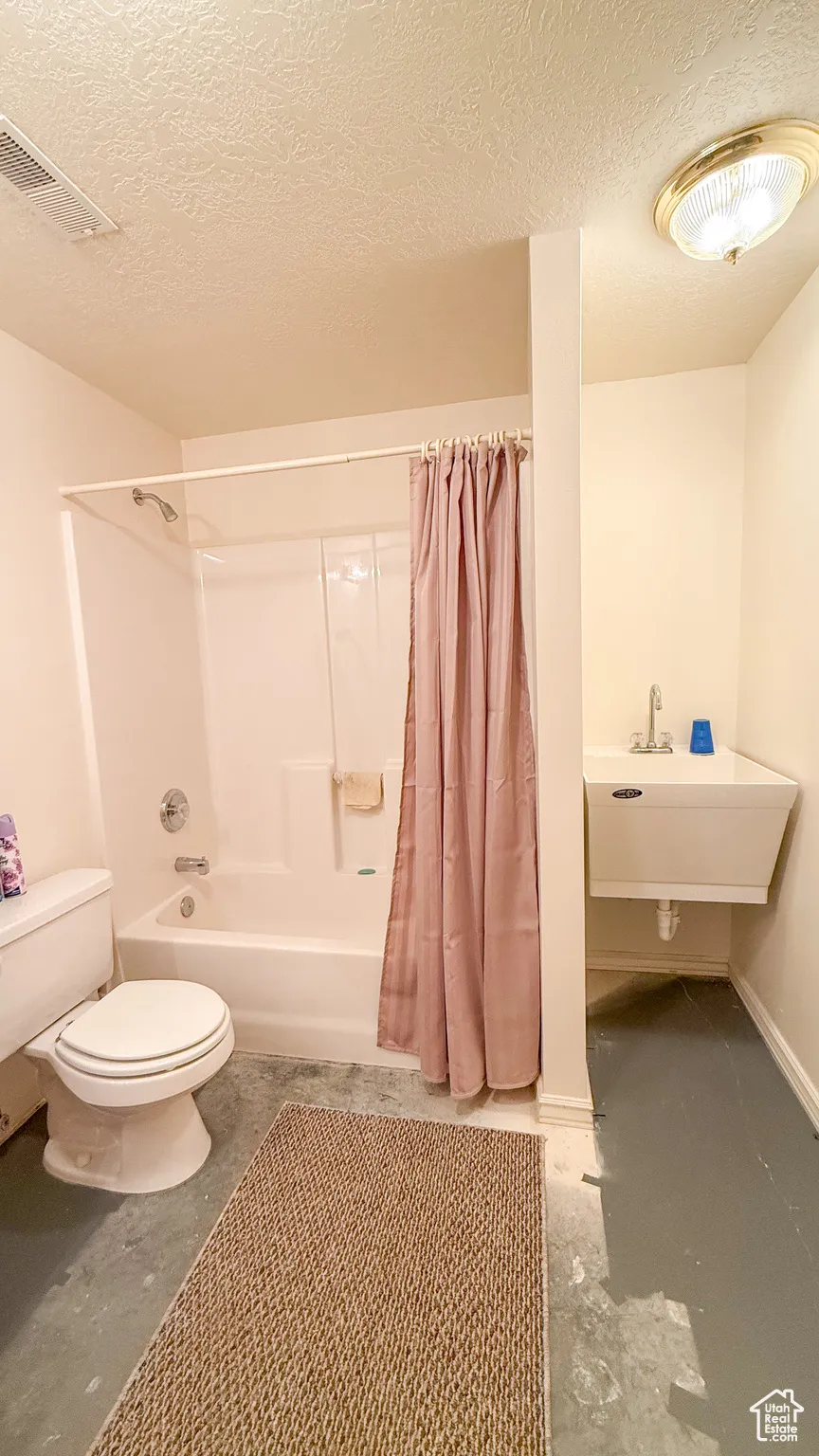 Bathroom featuring a textured ceiling, shower / tub combo, and concrete flooring