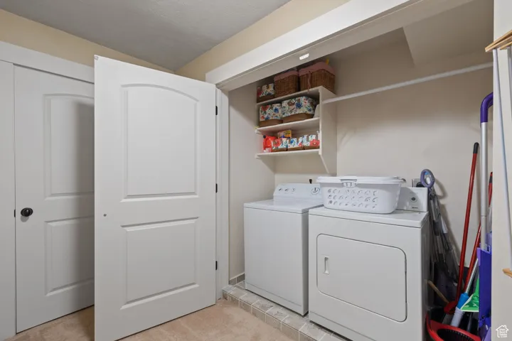 Laundry area with washing machine and clothes dryer, light carpet, and a textured ceiling