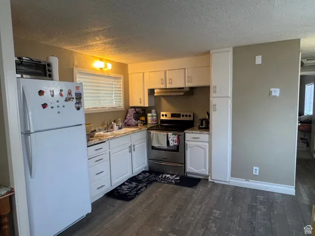 Kitchen featuring freestanding refrigerator, stainless steel range with electric stovetop, a textured ceiling, white cabinetry, and dark wood-style flooring