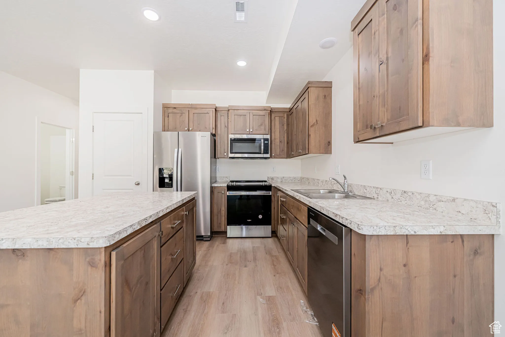 Kitchen featuring stainless steel appliances, light wood-style floors, a kitchen island, light countertops, and recessed lighting