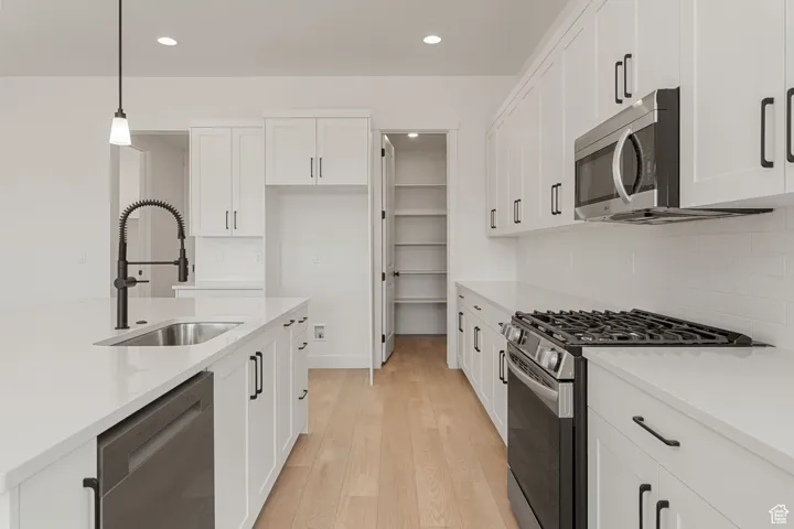Kitchen with appliances with stainless steel finishes, recessed lighting, white cabinetry, light wood-style floors, and light countertops