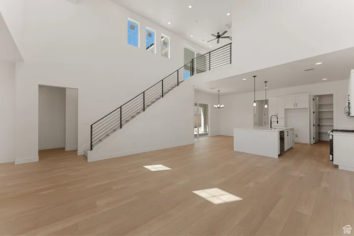Unfurnished living room featuring light wood-type flooring, stairs, ceiling fan, a chandelier, and recessed lighting