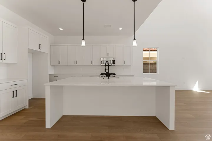 Kitchen with white cabinetry, a kitchen island with sink, light wood-style floors, light countertops, and backsplash