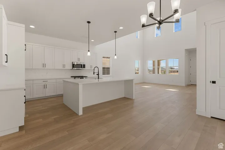 Kitchen with a chandelier, light wood-style floors, light countertops, decorative backsplash, and a center island with sink