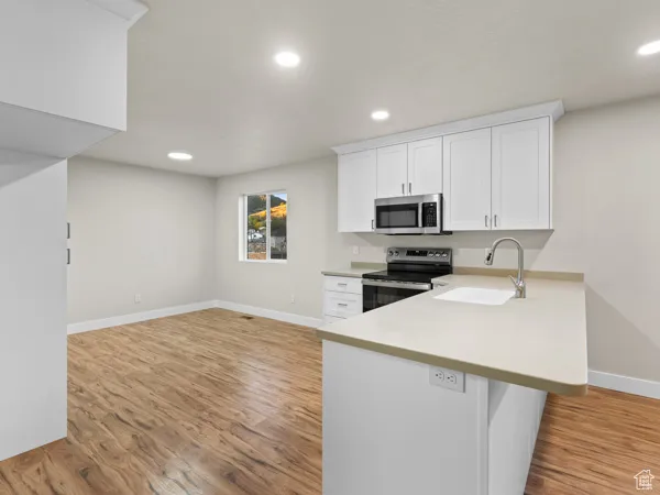 Kitchen with white cabinets, a peninsula, light countertops, stainless steel appliances, and light wood finished floors