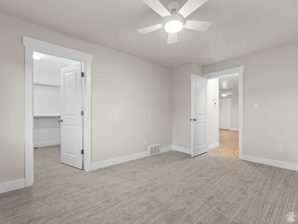 Unfurnished bedroom featuring light colored carpet, a walk in closet, and ceiling fan