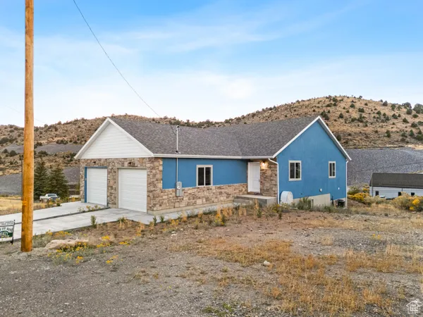 Ranch-style house featuring stucco siding, driveway, a garage, stone siding, and a mountain view