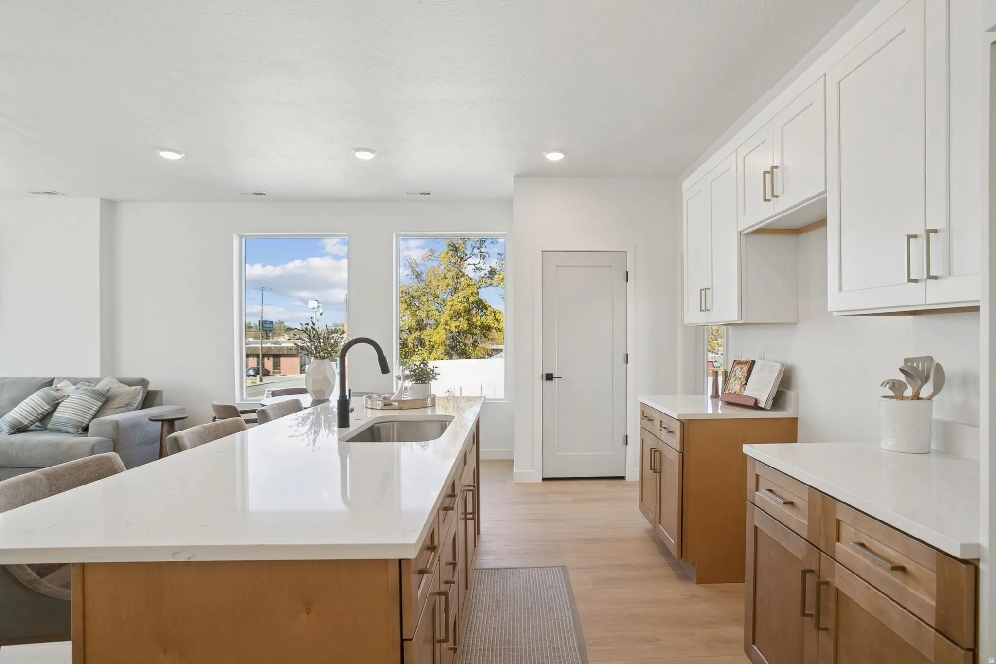 Kitchen featuring light wood-style flooring, light stone countertops, a kitchen island with sink, white cabinetry, and recessed lighting