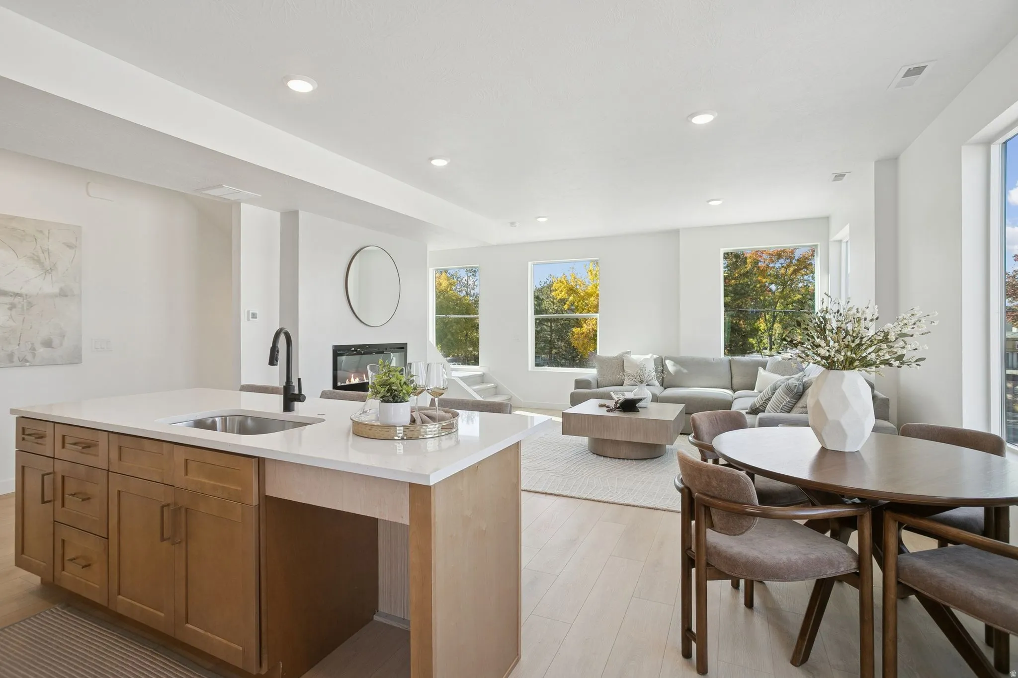Kitchen featuring brown cabinetry, a glass covered fireplace, light wood-style flooring, recessed lighting, and light stone counters