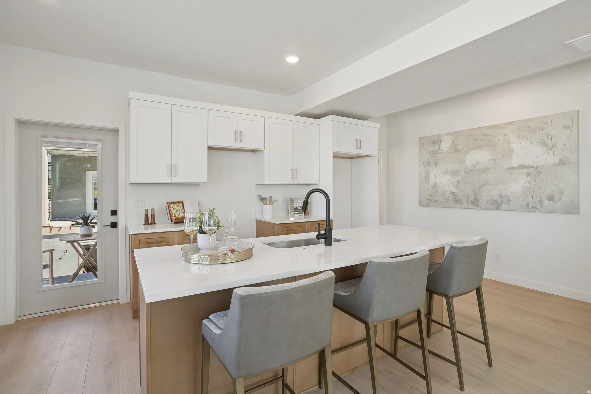 Kitchen featuring white cabinetry, light wood-style floors, light stone counters, recessed lighting, and a kitchen island with sink