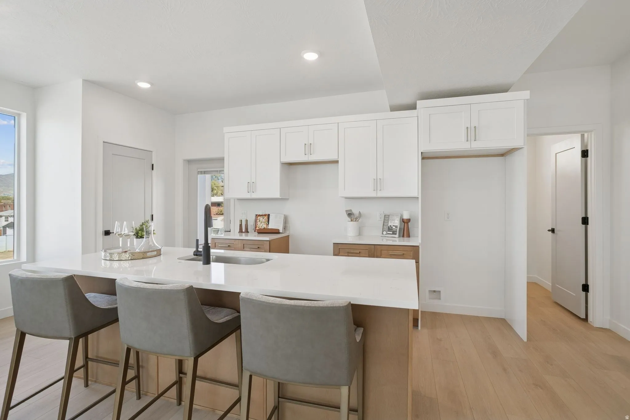 Kitchen with white cabinets, light stone countertops, light wood finished floors, a breakfast bar, and a center island with sink
