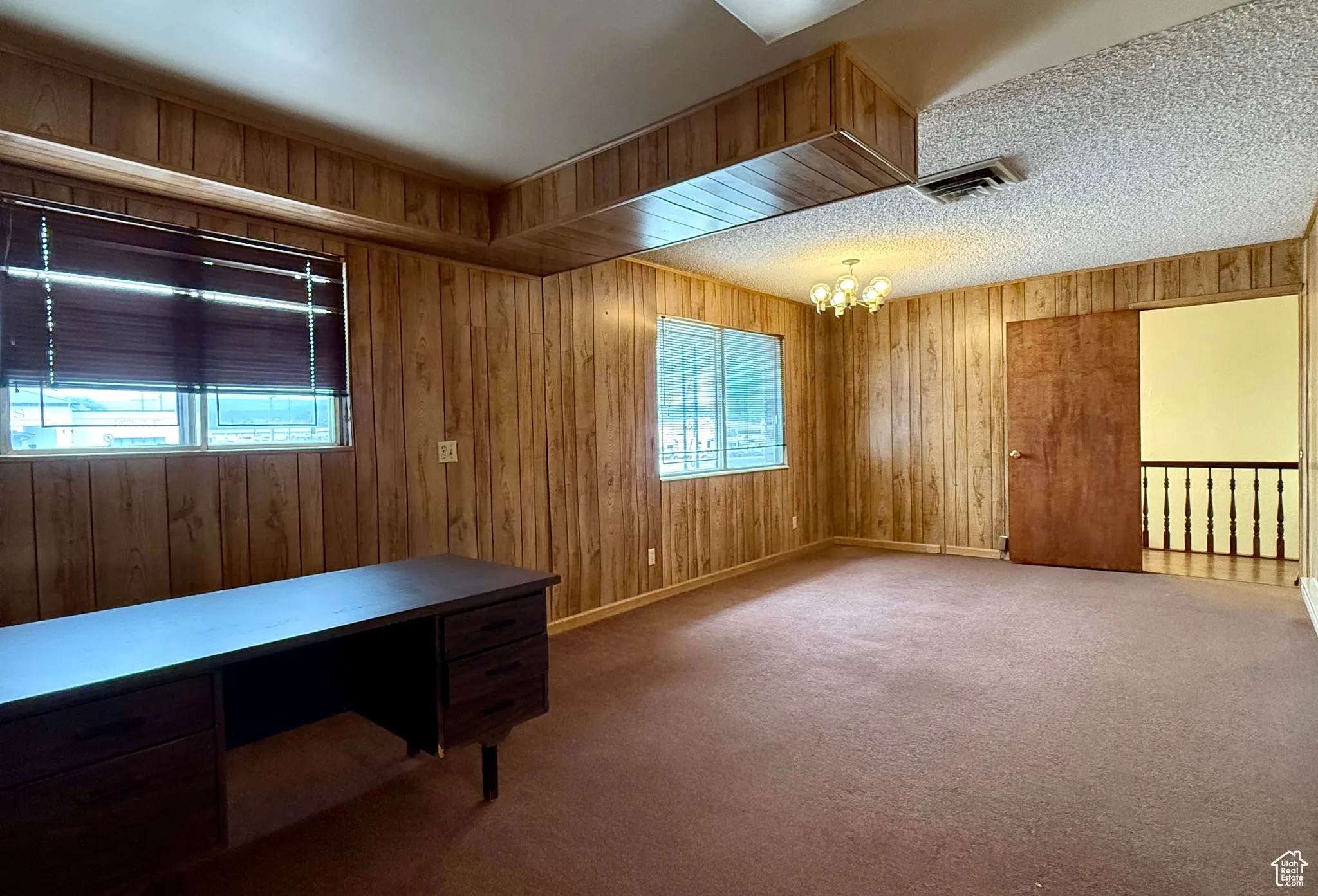 Unfurnished office with wooden walls, carpet floors, and a chandelier