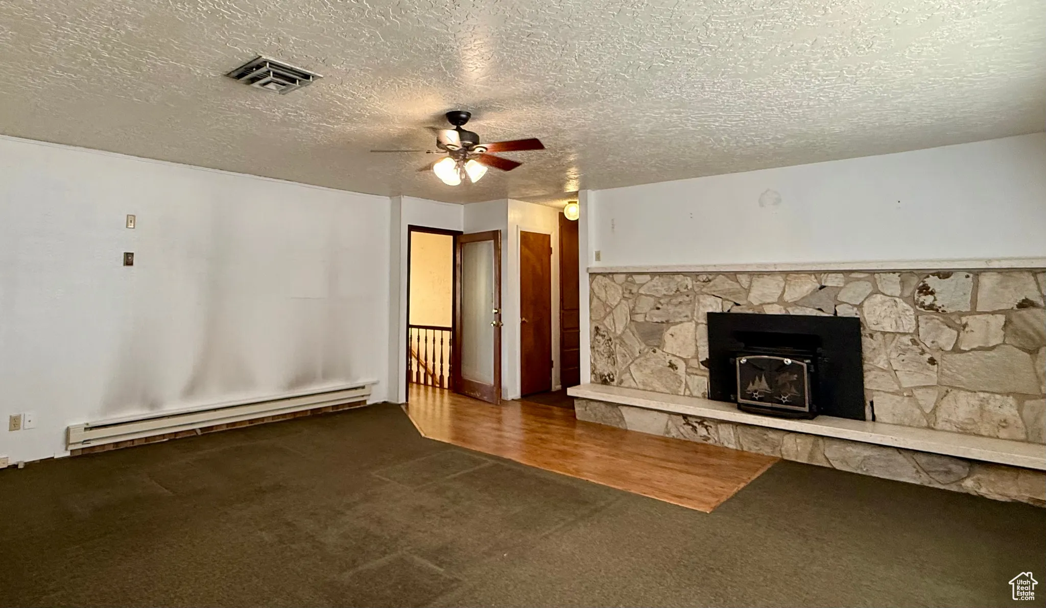Unfurnished living room featuring a baseboard heating unit, a ceiling fan, a textured ceiling, dark carpet, and a fireplace
