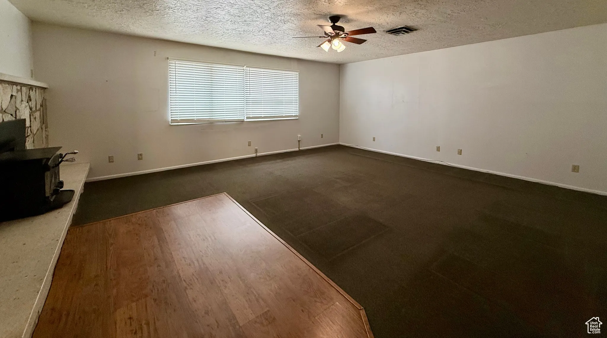 Unfurnished living room featuring a textured ceiling, dark wood-style flooring, a ceiling fan, and a wood stove