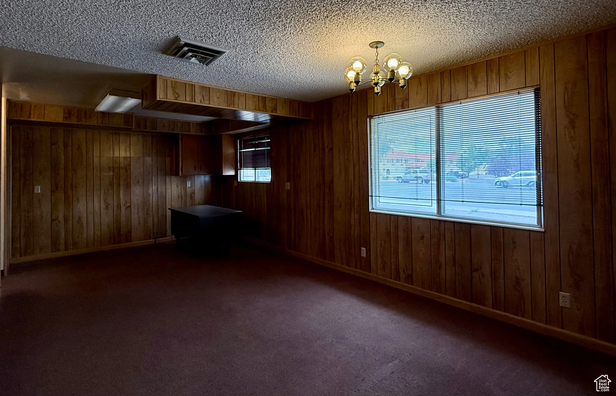 Spare room featuring wooden walls, a chandelier, dark carpet, and a textured ceiling