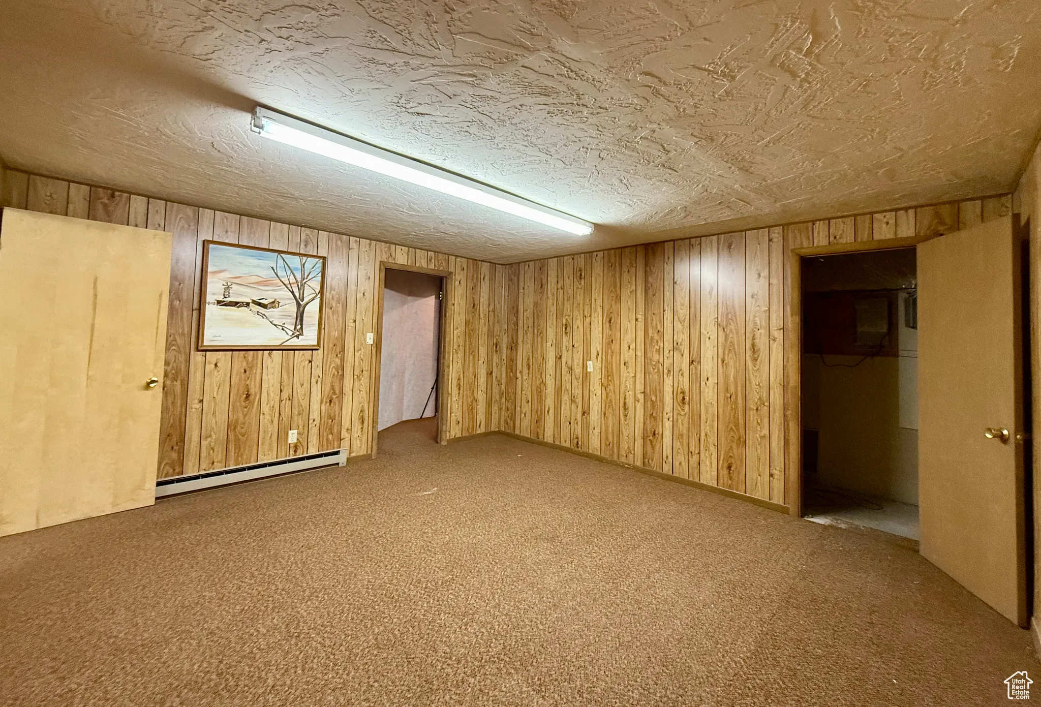 Finished basement with carpet flooring, wooden walls, a baseboard radiator, and a textured ceiling