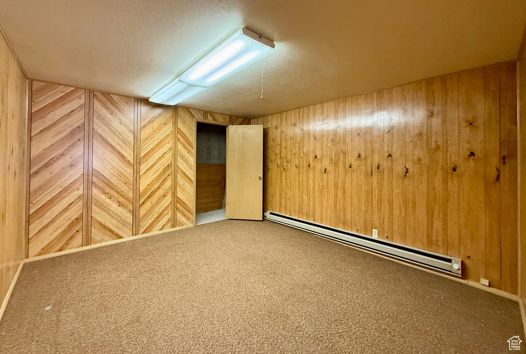 Carpeted spare room featuring a baseboard radiator, wood walls, and a textured ceiling