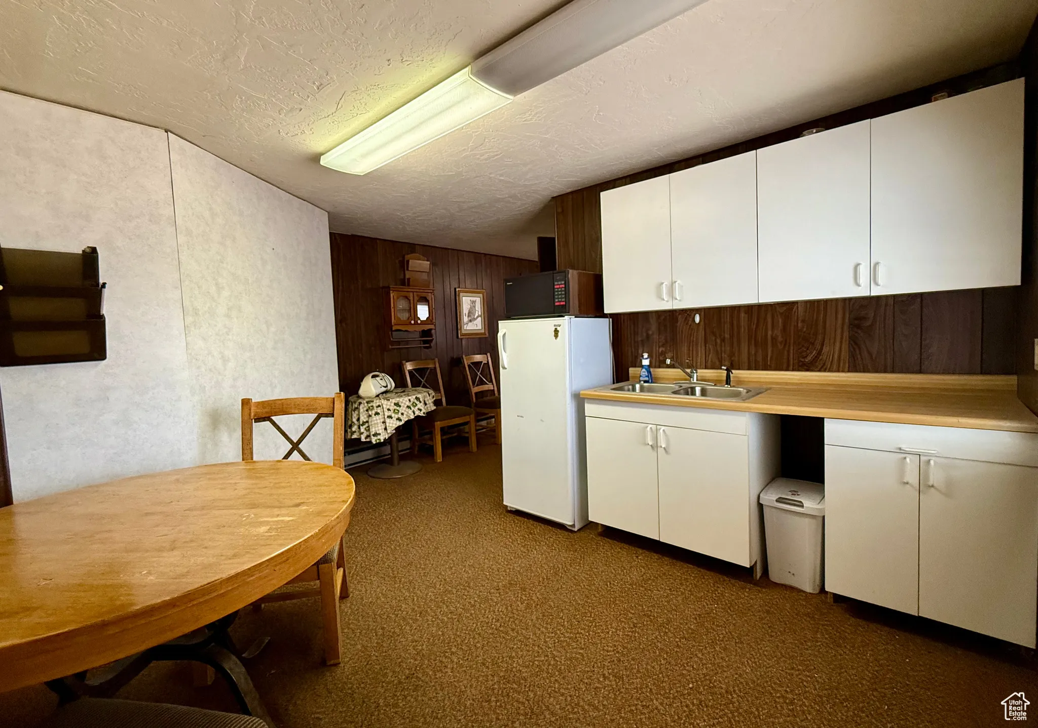 Kitchen with white cabinets, light countertops, freestanding refrigerator, wooden walls, and dark colored carpet
